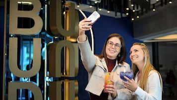 Two people taking a selfie with a large 'BUD' sign in the background.