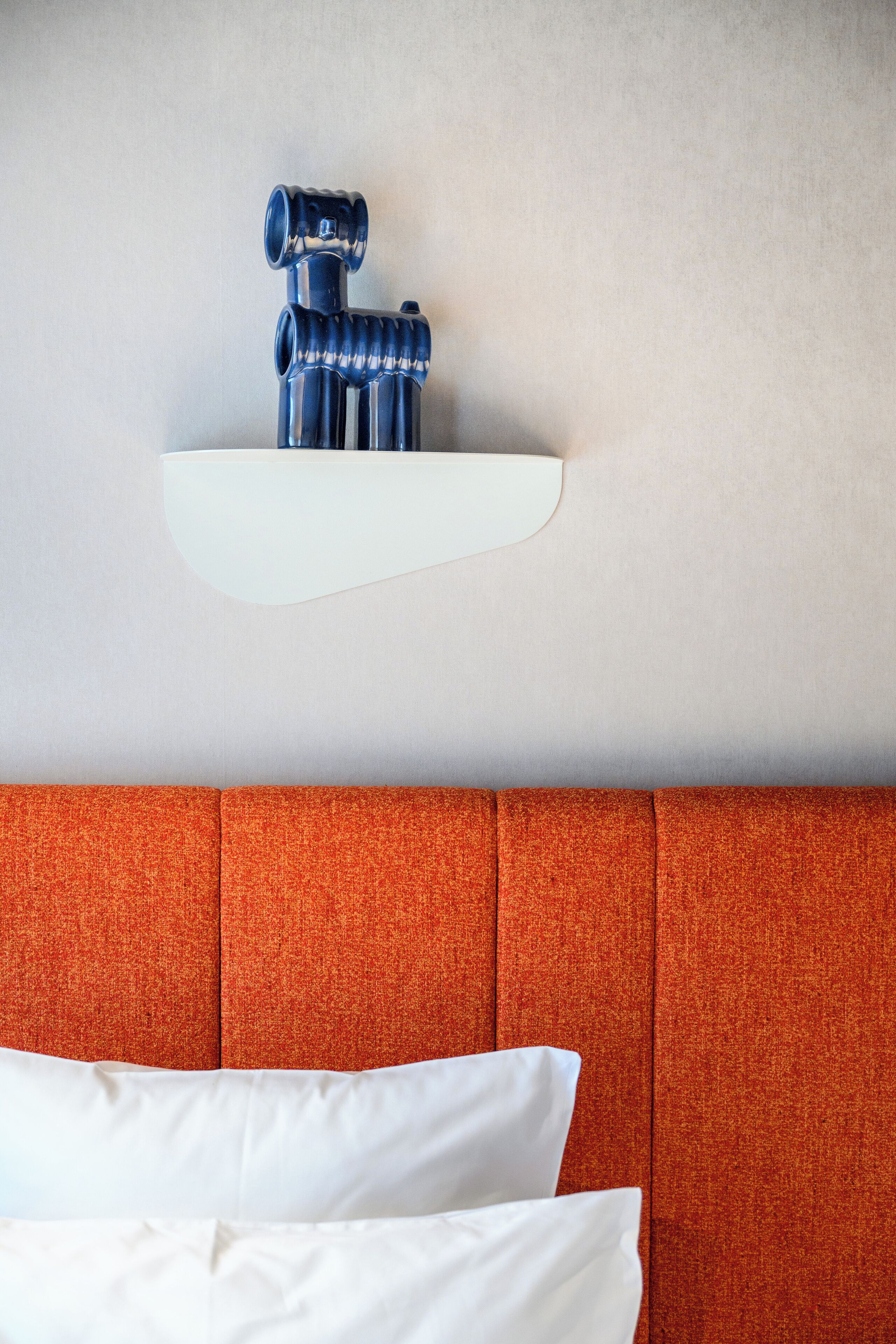 A hotel room with a white headboard, a red upholstered headboard, and a white pillow.