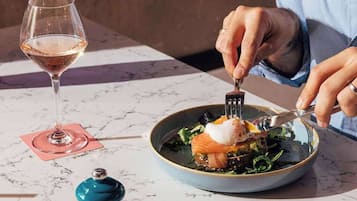 Una persona cenando en una mesa con una copa de vino y un plato de comida.