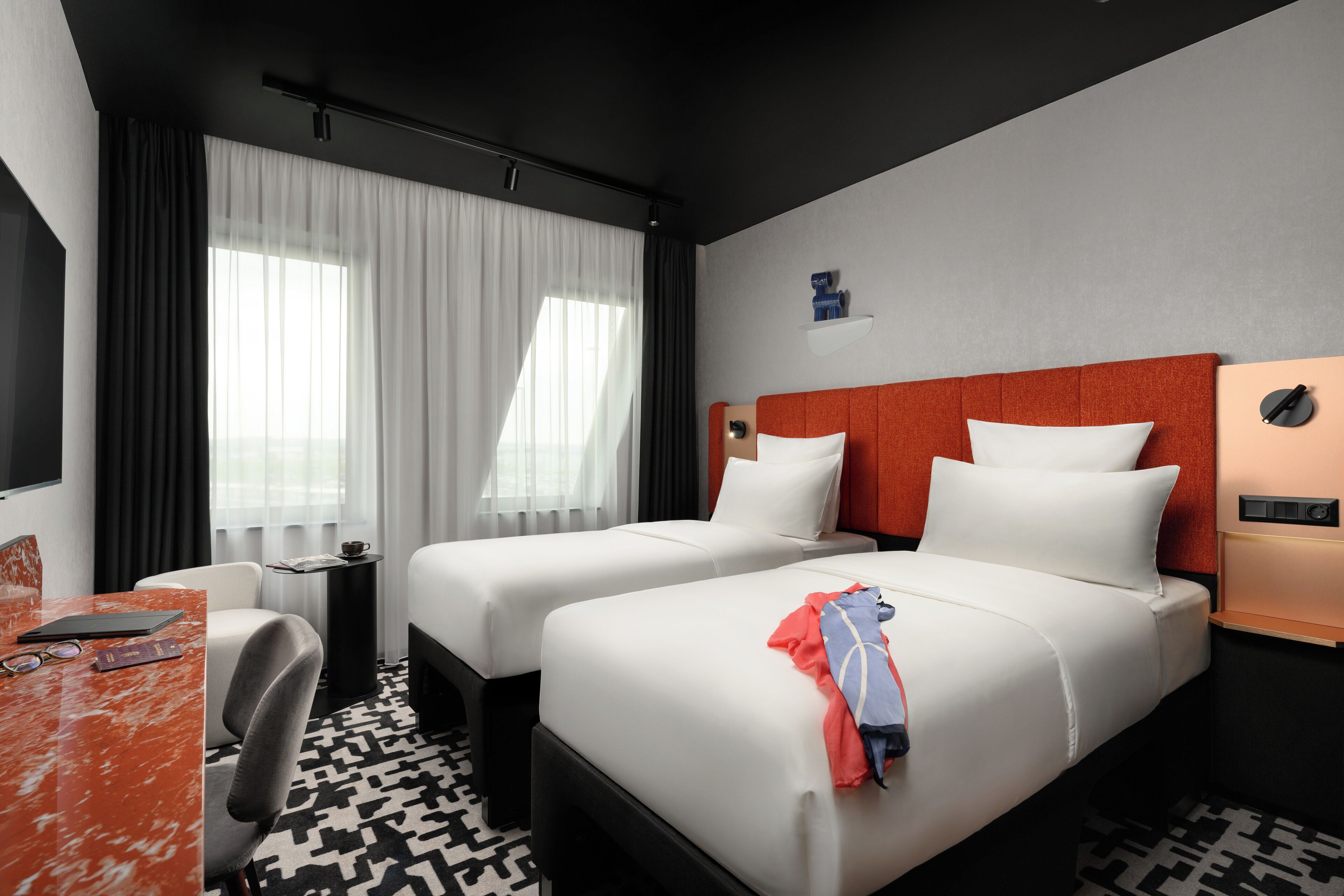 Habitación de hotel con dos camas, un escritorio, una silla, un televisor y una ventana con cortinas.