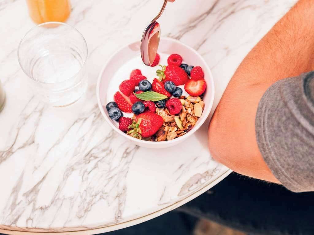 A bowl of cereal with fruits and granola on a marble table.