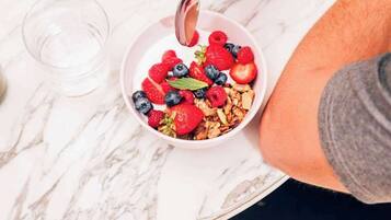A bowl of cereal with fruits and granola on a marble table.