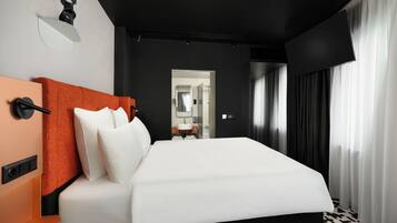 A modern hotel room with a large bed, a nightstand, a mirror, and a bathroom visible through an open door.