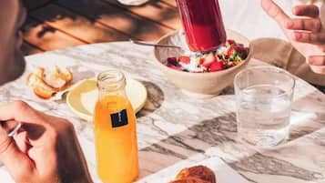 Una mesa de comedor con un tazón de ensalada, un vaso de agua, una botella de jugo de naranja y un pastel.