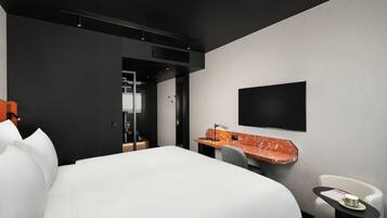 Habitación de hotel moderna con una cama grande, un escritorio con silla, un televisor de pantalla plana en la pared y una mesita con una taza.