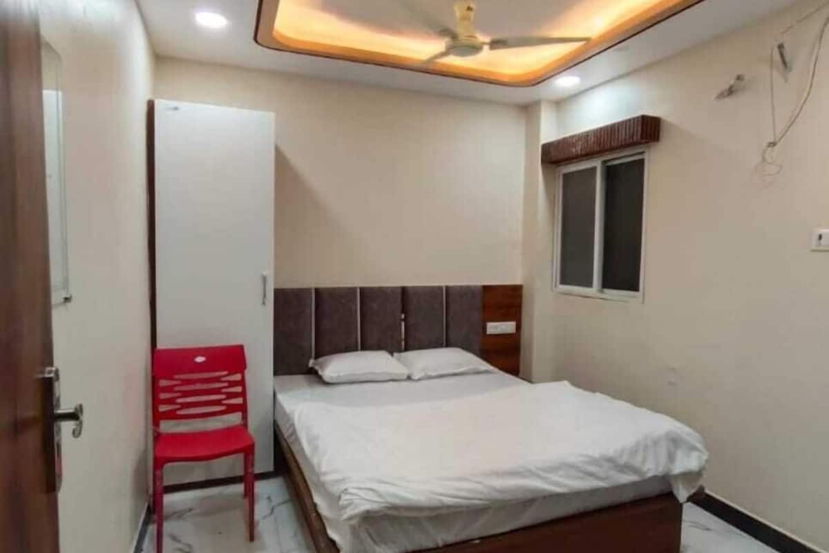 A bedroom with a bed, a red chair, a ceiling light fixture, and a window.