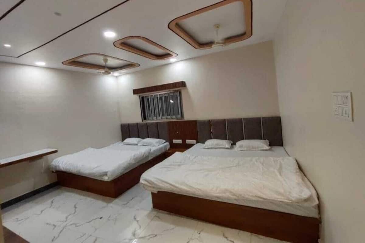 A bedroom with two beds, a wooden headboard, a window with bars, and a ceiling with recessed lighting.