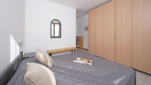 Une chambre à coucher comprenant un lit, une armoire en bois, un banc et un miroir fixé au mur.