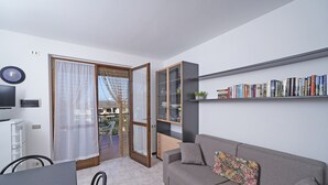 Un salon moderne avec un canapé gris, une bibliothèque et un coin repas comprenant une table et des chaises.