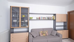 Un espace de vie compact comprenant un canapé gris, un meuble en bois doté de portes en verre et une bibliothèque.