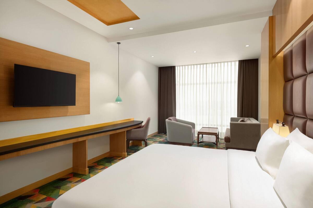 A hotel room with a bed, a desk, a chair, a television, and a window with curtains.