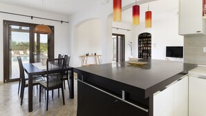 Una cocina moderna con una isla grande, luces colgantes y un comedor con mesa y sillas.