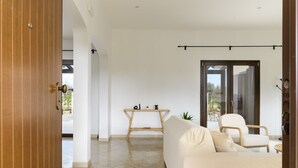 Un salón moderno con un sofá, una mesa y una silla. A la izquierda, una puerta de madera y, a la derecha, una puerta corrediza de vidrio.