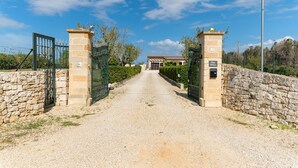 Un camino de grava conduce a una entrada con puerta, flanqueada por muros de piedra, bajo un cielo despejado.