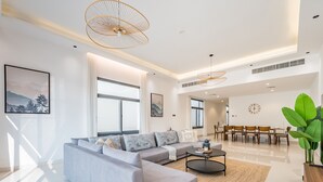 A modern living room with a grey sectional sofa, a coffee table, and a dining area with wooden chairs and a table. - Blue Marble Beach 4BR Villa with AsstRm,Private Pool and Access to Floating Pier (Fujairah)
