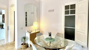 Un coin repas avec une table en verre entourée de chaises blanches, une petite plante en pot et un tapis noir.