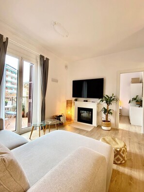 A modern living room with a fireplace, a flat-screen TV, and a balcony with outdoor furniture.