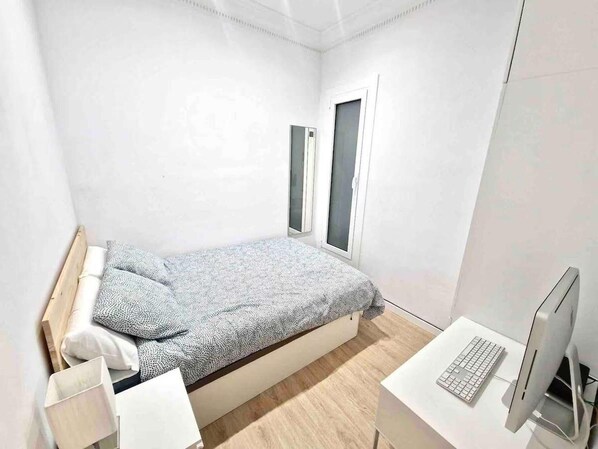 A small, modern bedroom with a bed, a desk, and a computer.
