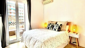 Une chambre à coucher comprenant un lit, une table de chevet, une lampe et une porte-fenêtre coulissante donnant sur un balcon.
