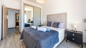 Une chambre moderne avec un grand lit, des tables de chevet, un miroir et un luminaire au plafond.