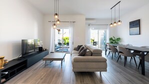 Un salon moderne doté d’un téléviseur à écran plat, d’un canapé, d’une table à manger avec des chaises et d’un éclairage suspendu.