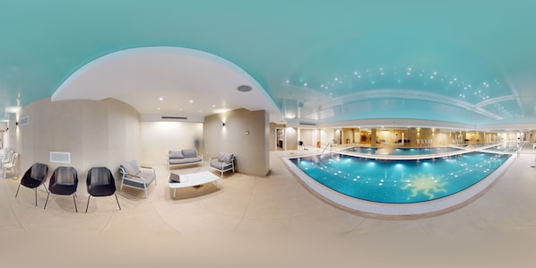 An indoor swimming pool with a curved design, seating area with chairs and a sofa, and a ceiling with a unique light fixture. - ★Prestigious King David 3BR/3BA - View! Pool & Gym★ (Jerusalem)