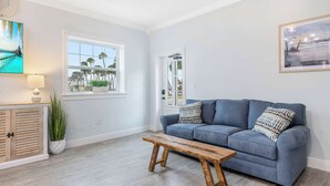 A living room with a blue sofa, a wooden bench, a potted plant, and a window with a view of palm trees. - Cozy Studio Condo in Sebastian! (Sebastian)