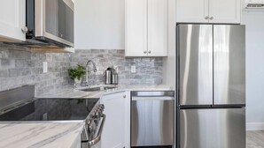 Una cocina moderna con armarios blancos, un refrigerador de acero inoxidable, un horno integrado y una estufa negra.
