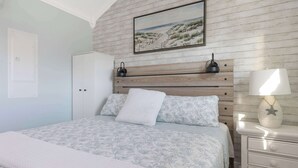 Un dormitorio con cama, mesita de noche, lámpara, armario y un cuadro en la pared.