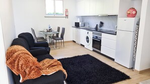 Moderni keittiö, jossa on valkoiset kaapit, sisäänrakennettu uuni ja jääkaappi. Keittiössä on ruokailutila, jossa on pöytä ja tuolit, ja lattialla on musta matto.