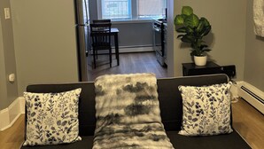 A living room with a sofa, two decorative pillows, a potted plant, and a clock on the wall.