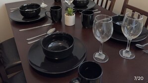 A dining table set with black plates, bowls, and wine glasses, with a small potted plant in the center.