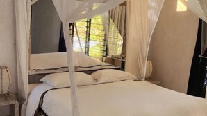 A bed with a canopy, a bedside table, and a window with blinds. - Malindi Marine Park 3 bedroom BeachFront (Malindi)