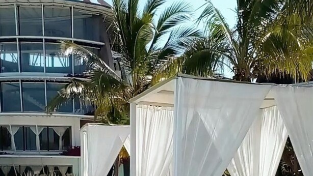 A resort with white canopy beds, palm trees, and a modern building in the background. - Malindi Marine Park 3 bedroom BeachFront (Malindi)