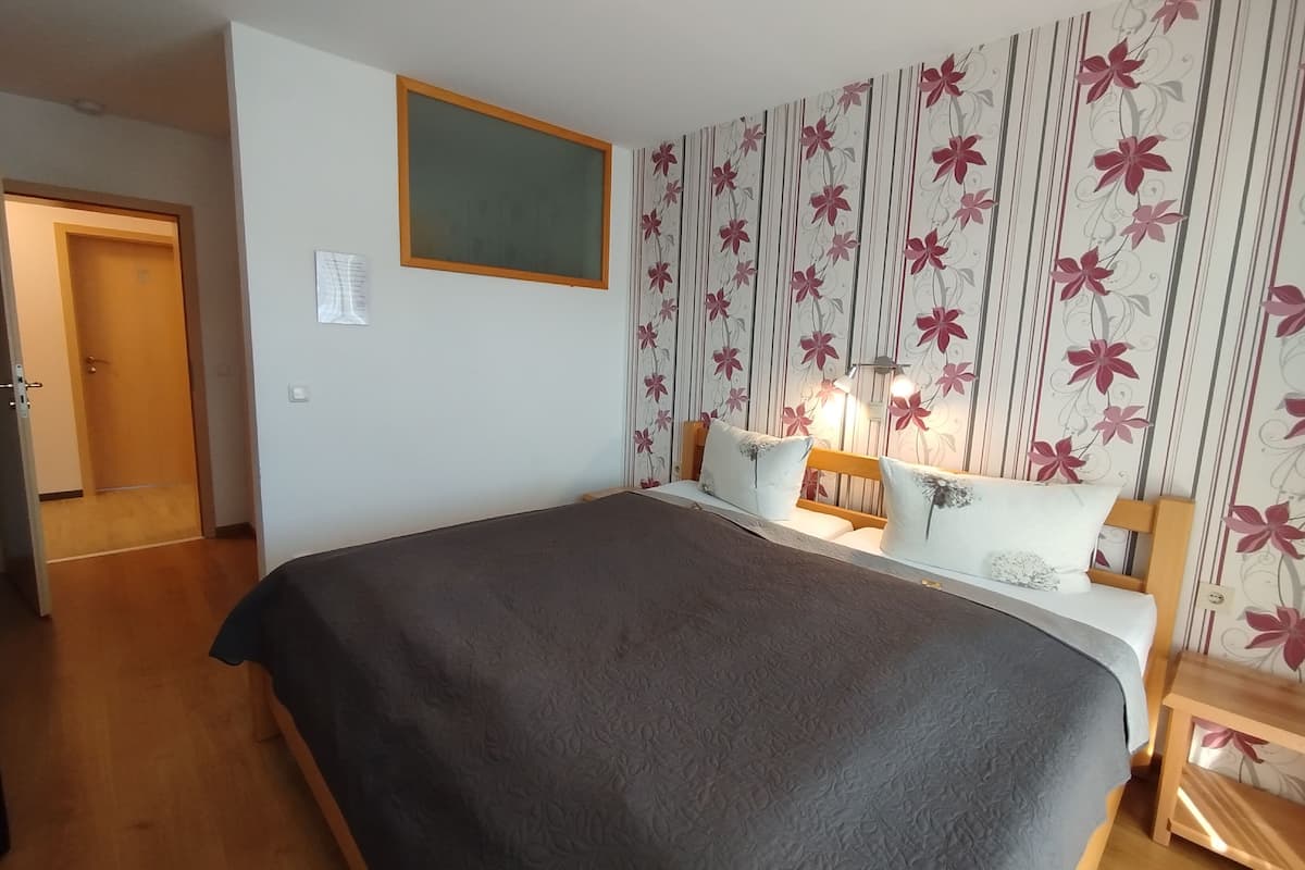 Ein Schlafzimmer mit Bett, Nachttisch, Lampe und Fenster.