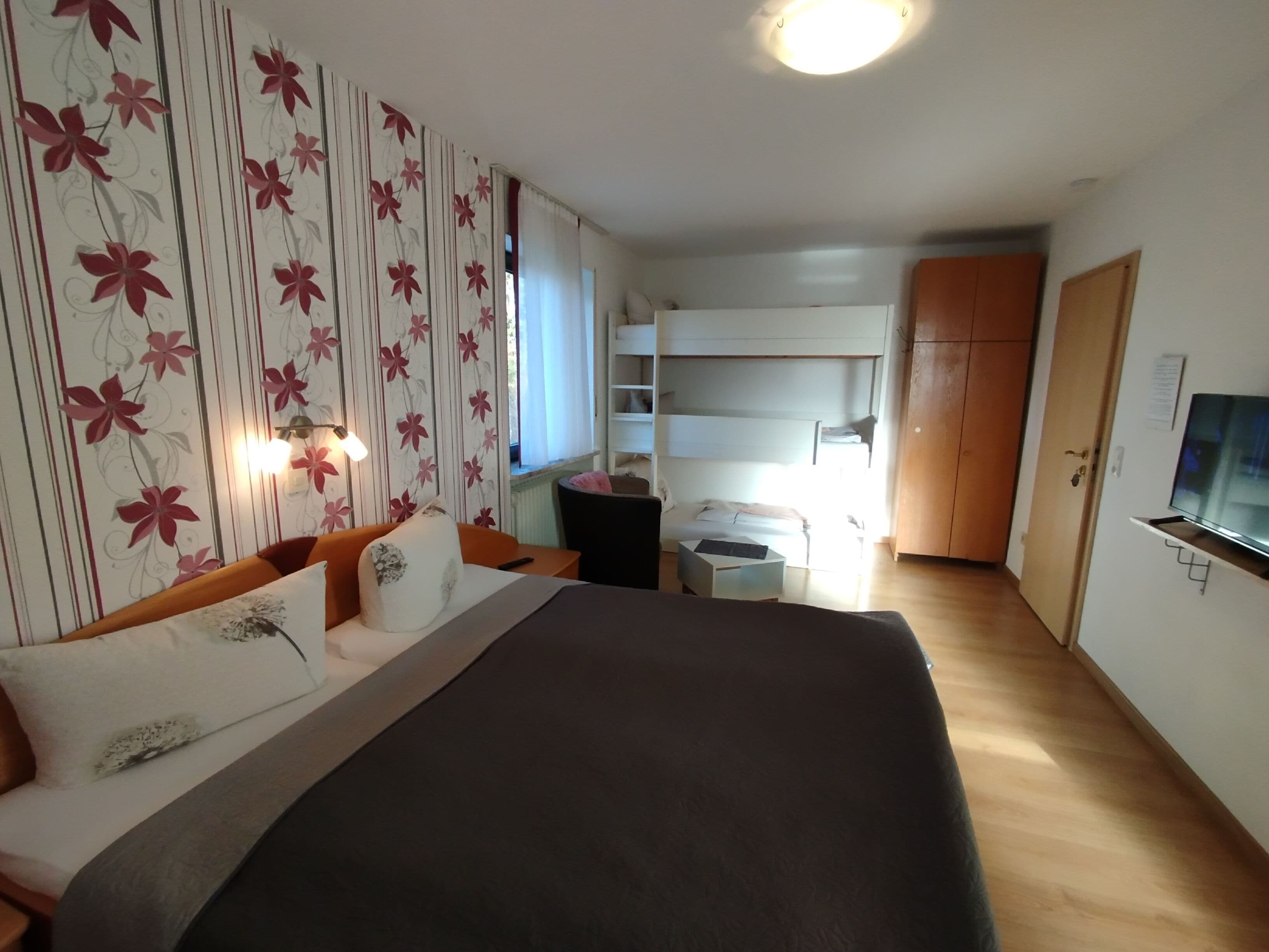 A bedroom with a large bed, a bedside table, a wardrobe, a TV, and a window with curtains.