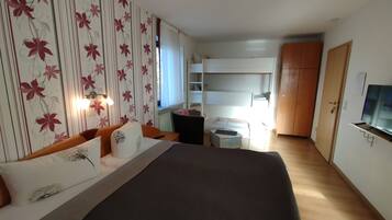A bedroom with a large bed, a bedside table, a wardrobe, a TV, and a window with curtains.