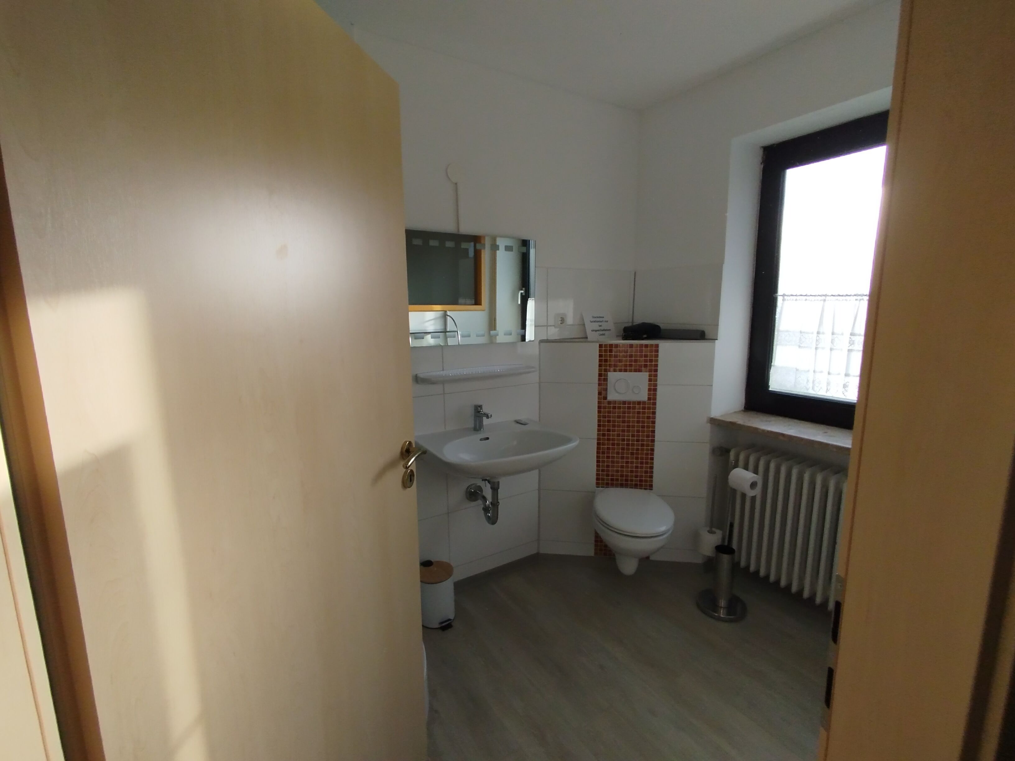A small, clean bathroom with a sink, toilet, and window.