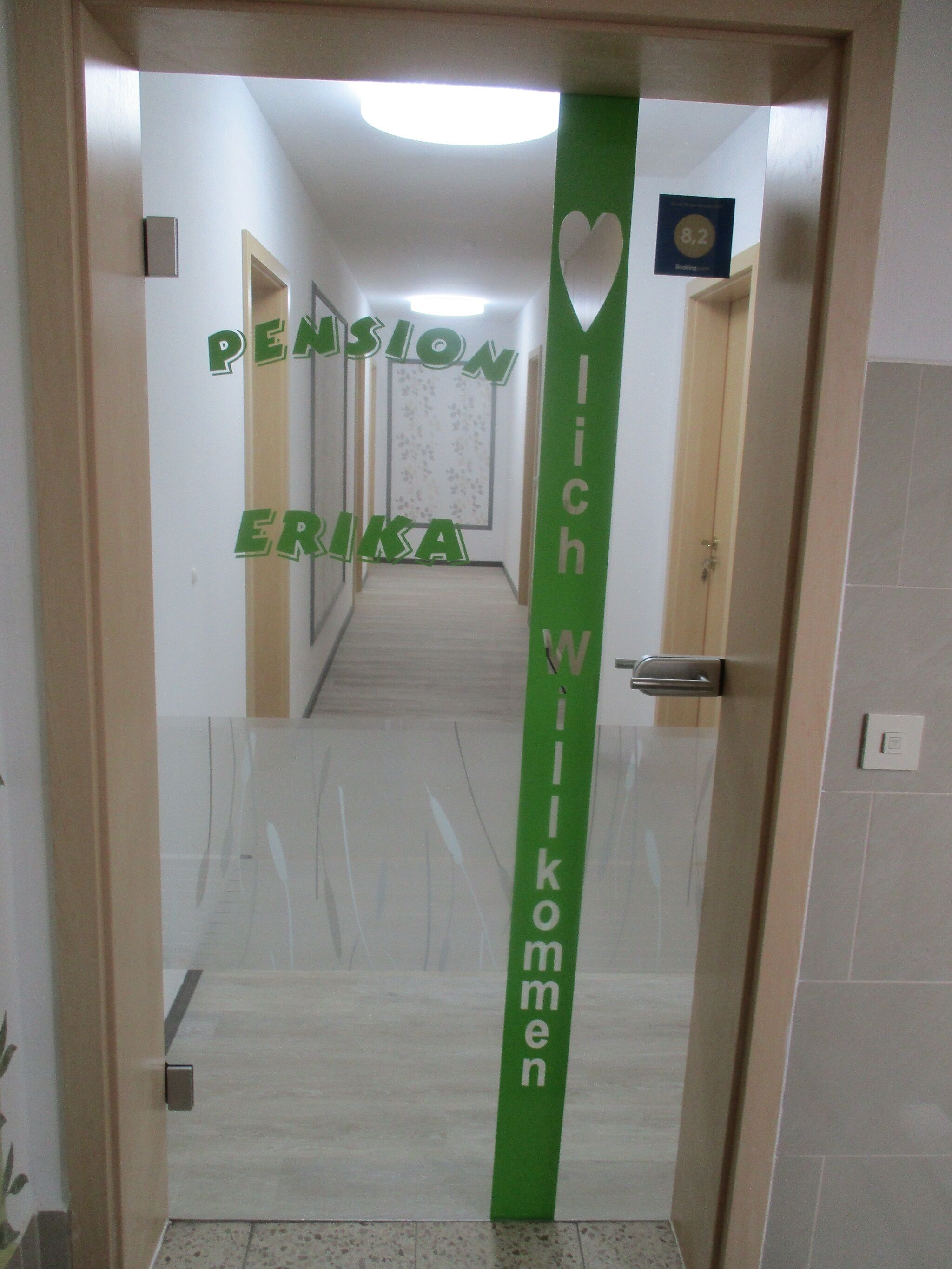 A hotel entrance with a green sign reading "PENSION ERIKA" and "Wilkommen" (Welcome).