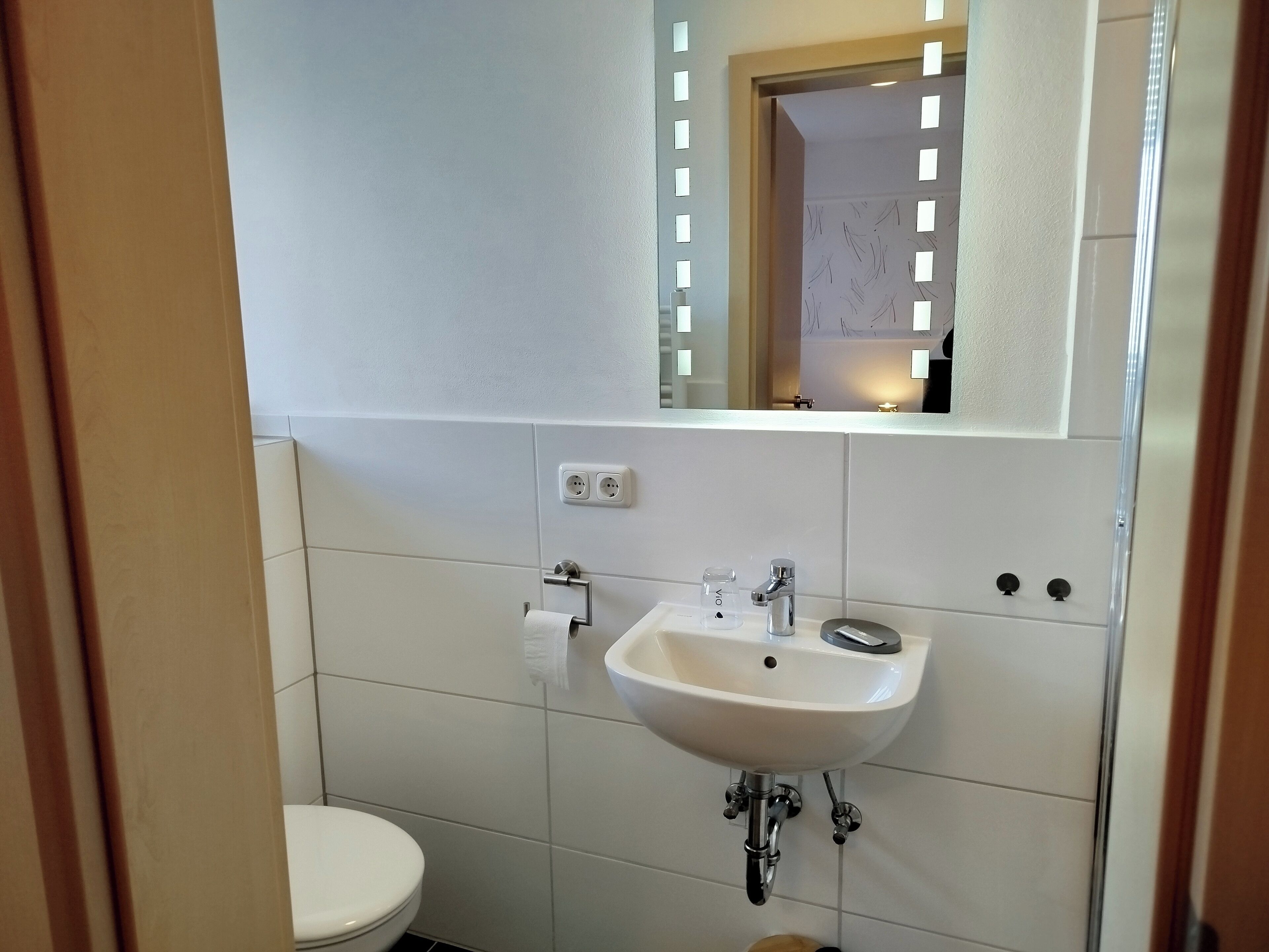 Un baño con un lavamanos blanco, un inodoro y un espejo sobre el lavamanos.