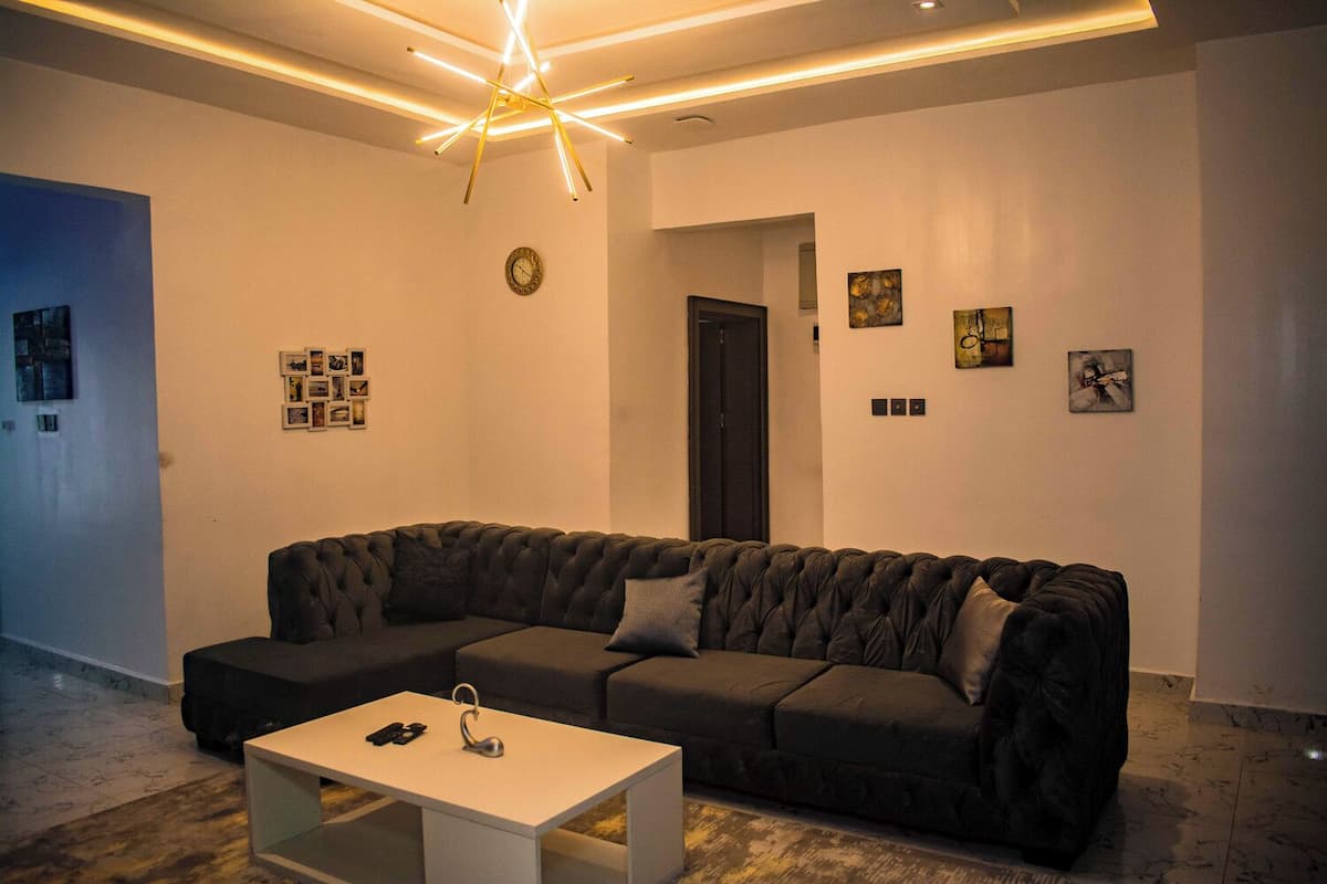 Una sala moderna con un sofá modular gris oscuro, una mesa de centro blanca y una lámpara de techo original.