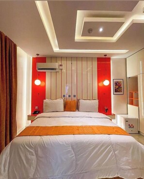 Een moderne hotelkamer met een groot bed, rode accentmuren, een airconditioningapparaat, een nachtkastje met een lamp en een lijst met een afbeelding aan de muur.