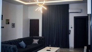 Uma sala de estar moderna com um sofá de cor escura, uma mesa de centro branca e um lustre geométrico singular.