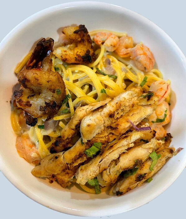 A bowl of food with grilled chicken, shrimp, and noodles.