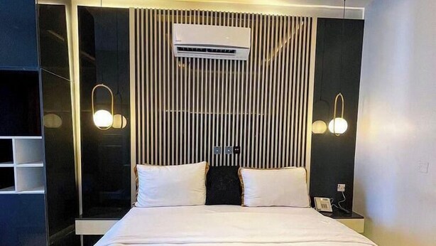 Quarto de hotel moderno com uma cama grande, guarda-roupa embutido, televisão de tela plana e mesa de cabeceira com abajur.