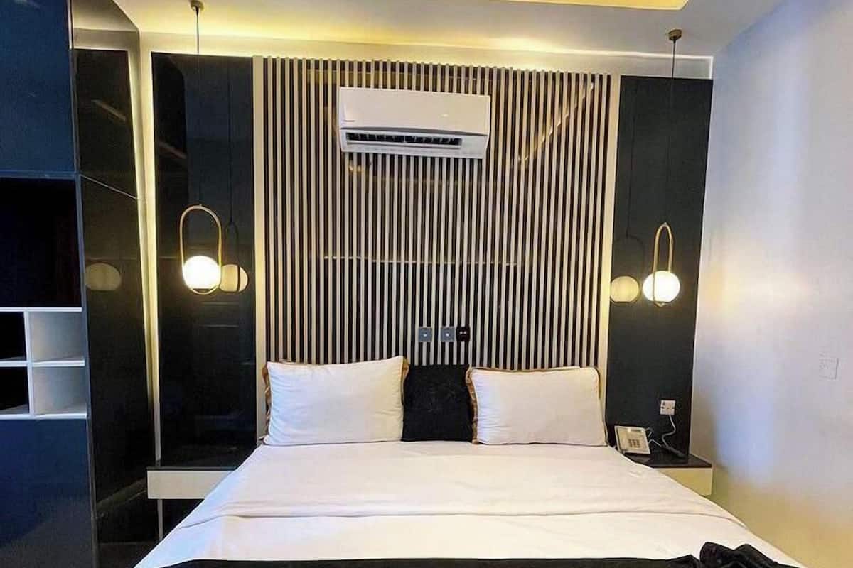 Una habitación de hotel moderna con una cama grande, un armario empotrado, un televisor de pantalla plana y una mesita de noche con lámpara.