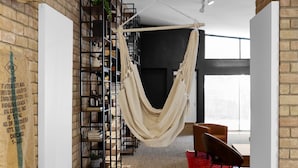 Een kamer met een bakstenen muur, een hangmat, een wit roomdivider, een houten tafel en een boekenkast.