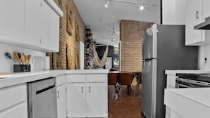 Een moderne keuken met witte kastjes, een bakstenen muur en een eethoek met tafel en stoelen.
