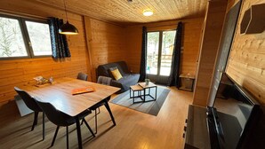 A cozy cabin interior with a wooden dining table, a sofa, and a TV. - Cocooning riverside Chalet on a small campsite in the Heart of Auvergne (Saint-Bonnet-de-Condat)