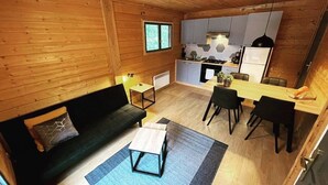 A compact living space with a wooden interior, a sofa, a dining table, and a kitchenette. - Cocooning riverside Chalet on a small campsite in the Heart of Auvergne (Saint-Bonnet-de-Condat)
